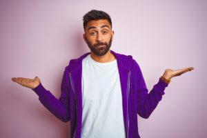 Young indian man wearing purple sweatshirt standing over isolated pink background smiling showing both hands open palms, presenting and advertising comparison and balance