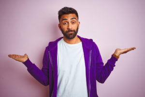 Young indian man wearing purple sweatshirt standing over isolated pink background smiling showing both hands open palms, presenting and advertising comparison and balance