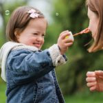 autistic child holding bubble wand near face of mother in park